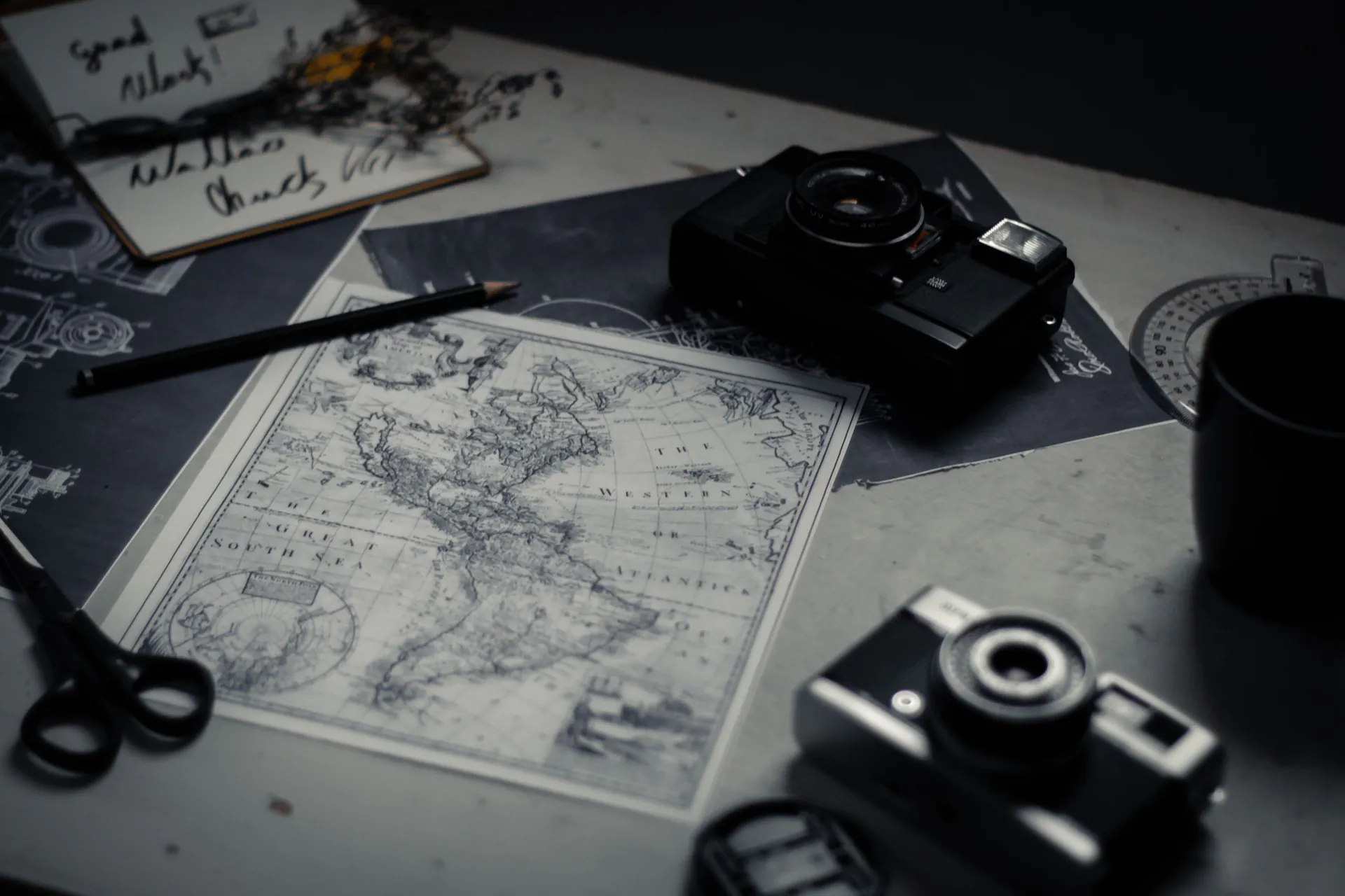 Two vintage film cameras on a dark desk with a map, pencil and notes
